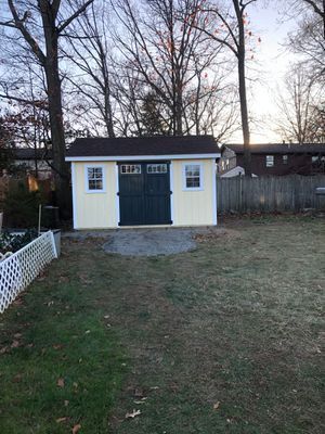 Yellow shed with brown roof and green doors in a backyard.