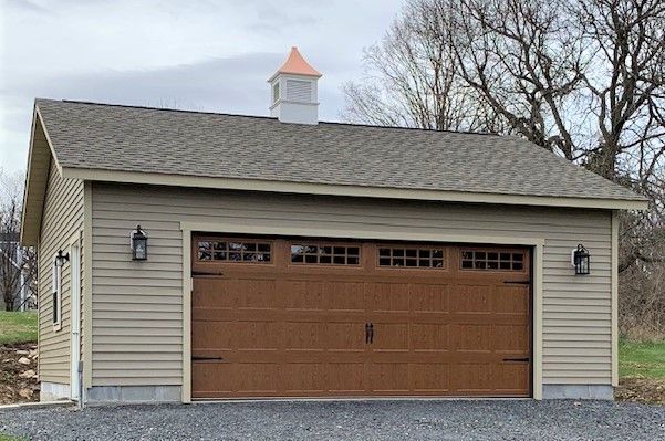 Tan-sided garage with brown garage door, cupola, and two black sconces.