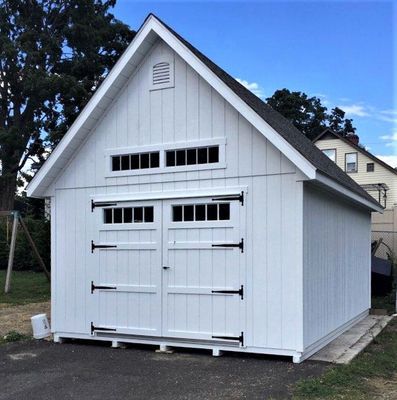 White shed with a gable roof, black hardware, and small windows.