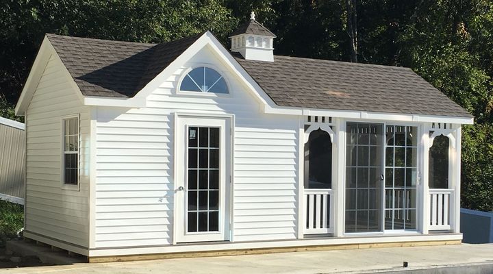 White garden shed with dark roof, arched window, and glass sliding doors.