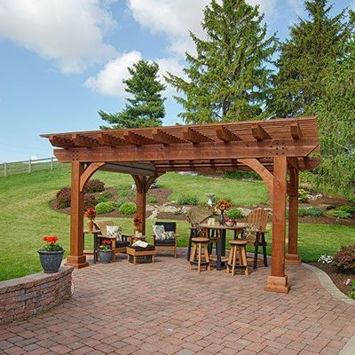 Wooden pergola over a brick patio with outdoor seating, surrounded by a lawn, flowers, and trees.