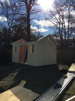A partially built shed in a yard with unfinished siding and a framed door.