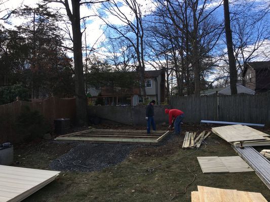 Two people building a shed in a backyard, surrounded by trees, with wooden planks and materials.