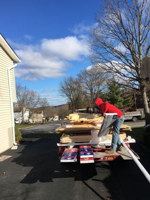 Person in red hoodie unloading lumber from trailer on a sunny day.