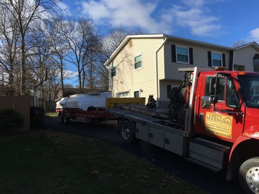 A red tow truck with a boat on a trailer parked in front of a two-story house on a sunny day.