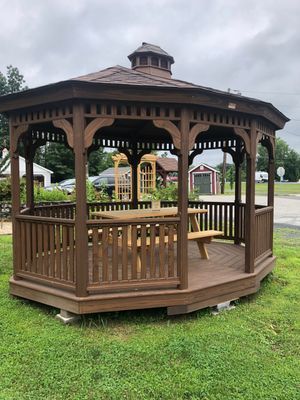 Brown octagonal gazebo with benches on a grassy lawn under an overcast sky.