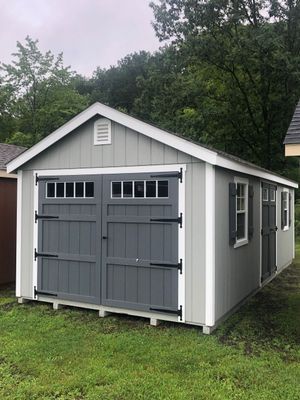 Gray shed with double doors, white trim, and small windows, set on grass.