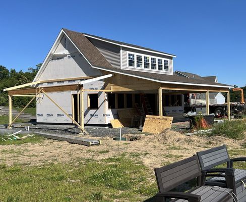 House under construction with gray siding, brown roof, and covered porch. Construction materials on site.