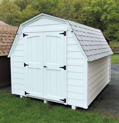 White barn-style shed with black door hardware, gray roof, and wooden siding, on green grass.
