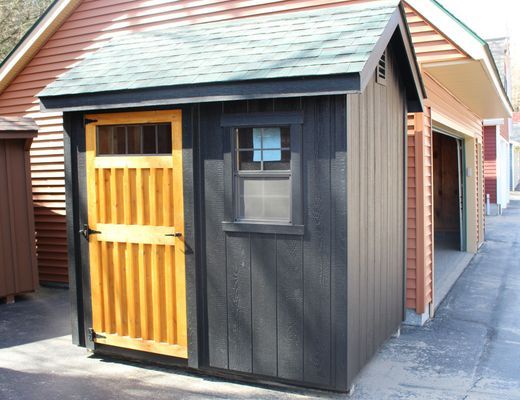 Black shed with wood door and window, next to a garage.
