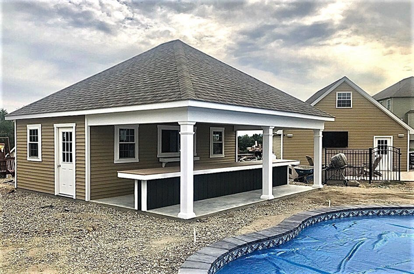Poolside building with outdoor bar, tan siding, gray roof, and pool in front.