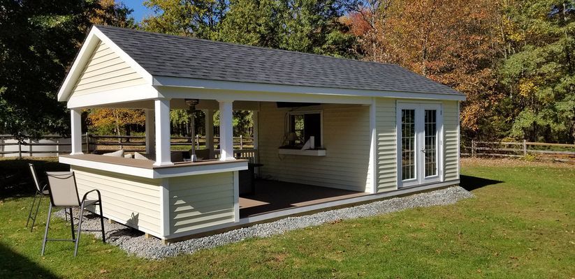 A small light yellow building with a bar area and a deck on a grassy lawn.