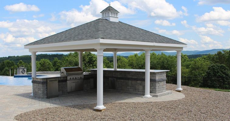 Gazebo with outdoor kitchen: white pillars, gray roof, stone facade, overlooking pool and mountains.