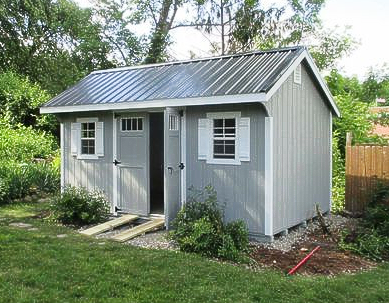 Green shed with orange trim and doors, small window, and a dormer.