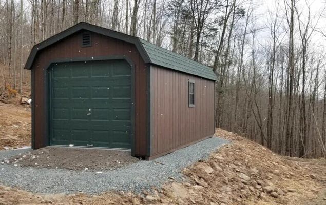 Brown garage with green door and roof, gravel path, trees in background.