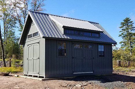 Grey shed with metal roof, double doors, and windows, set outdoors on a sunny day.