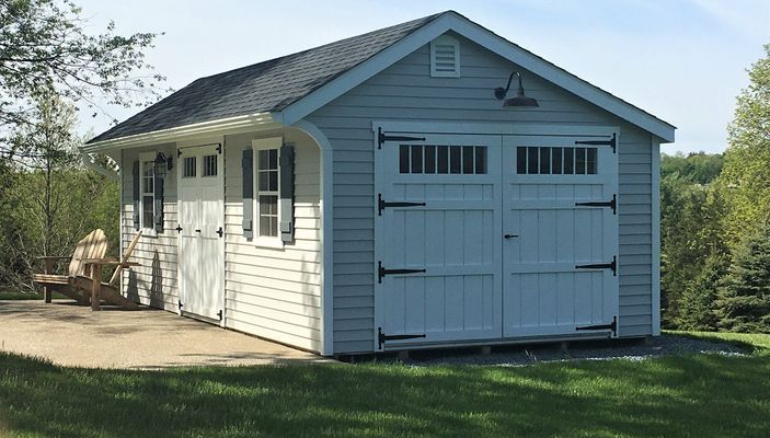 Light blue shed with white garage doors, black hardware, and a dark shingled roof.