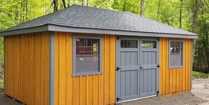 Yellow shed with gray door, trim, and roof in a wooded area.