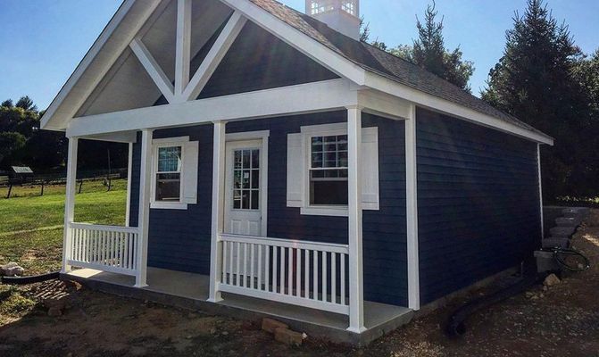 Blue cottage with white trim and porch, set in a field.