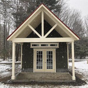 Small cabin with red roof and white trim, snow-covered ground, and trees in the background.