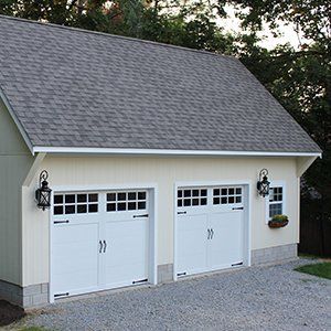 Two-car garage with white doors, light-colored walls, gray roof, and gravel driveway.