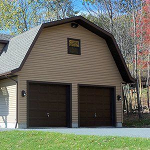 Two-car garage with brown doors and tan siding, set against a wooded backdrop.