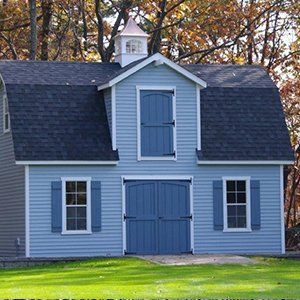 Blue barn with dark blue roof, doors, and shutters, set in a yard with trees.