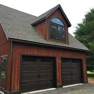 Two-car garage with brown doors, wood siding, and a dormer window.