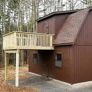 Brown two-story building with a wooden deck. It has a brown roof, two windows, and a light brown deck with railings.