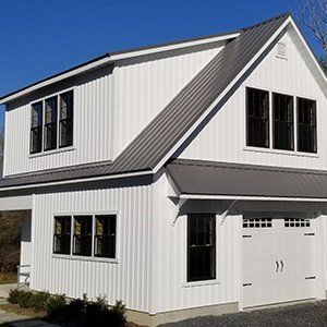 Two-story white farmhouse with black-trimmed windows and a gray metal roof on a sunny day.