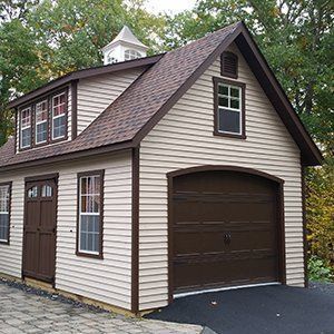 Tan two-story garage with brown trim, door, and garage door.  White cupola on the roof.
