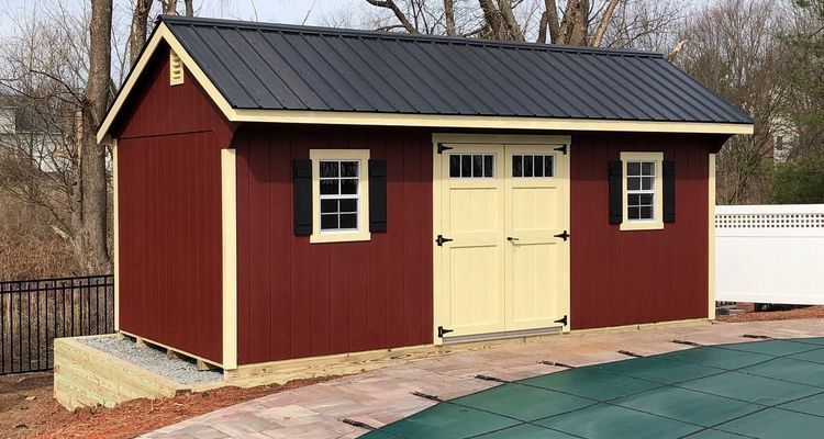 Red storage shed with black roof and cream-colored door and window frames, next to a pool.