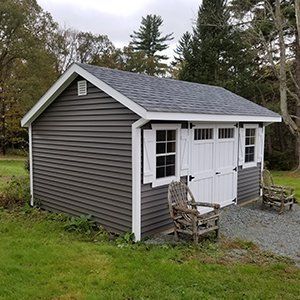 Dark gray shed with white trim, doors, and shutters, in a grassy yard.