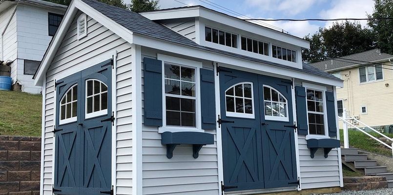 Blue and white shed with arched door details, shutters and window boxes.