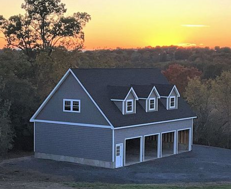 Tan building with green roof, garage door, windows with green shutters, and outdoor lights.
