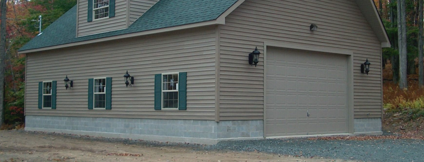 Tan building with green roof, garage door, windows with green shutters, and outdoor lights.