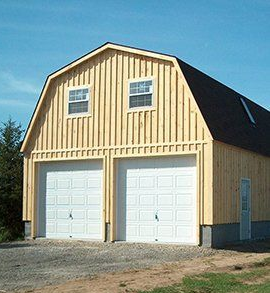 Two-car wooden garage with white doors and a gambrel roof, on a gravel driveway.