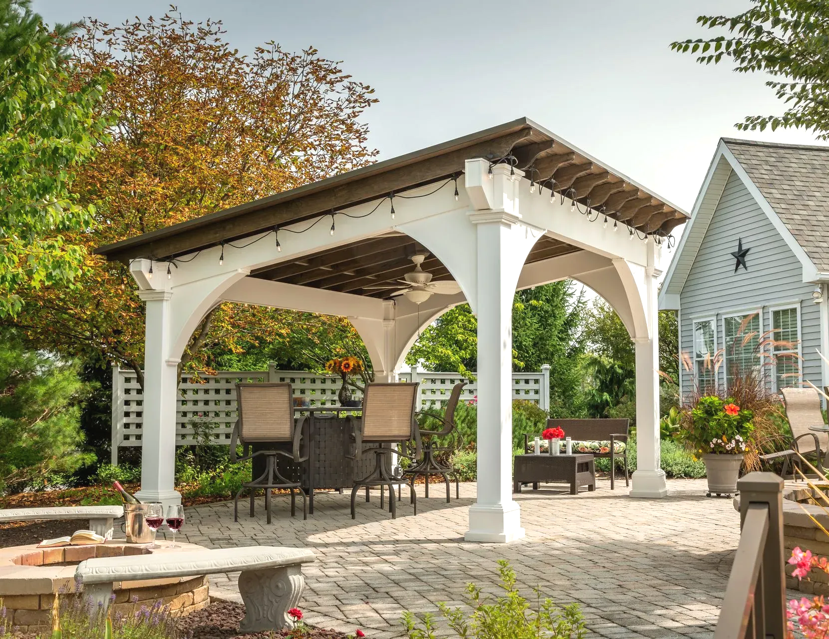 Outdoor kitchen with a wooden roof, grill, and pizza oven on a patio.
