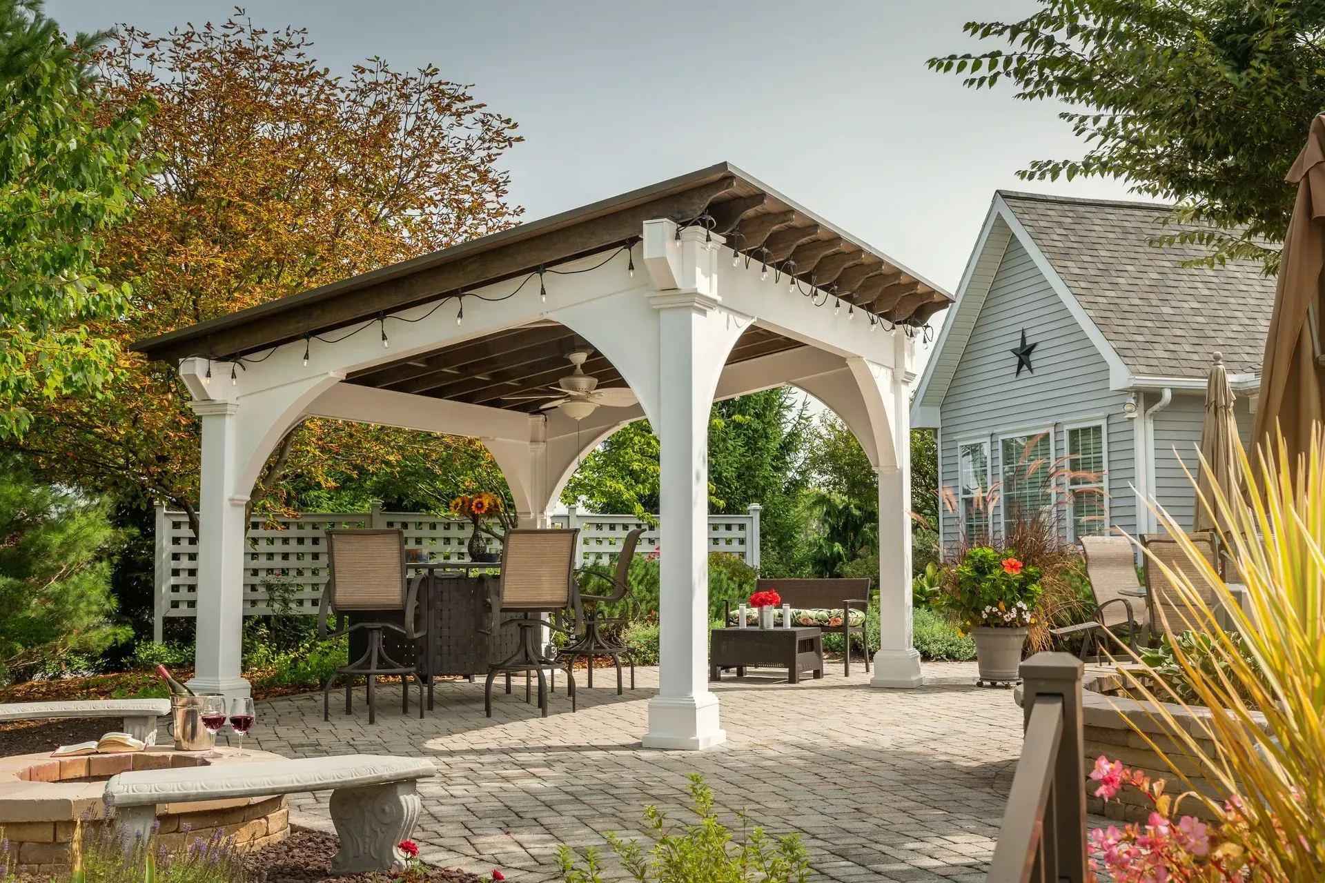 Outdoor kitchen with a wooden roof, grill, and pizza oven on a patio.