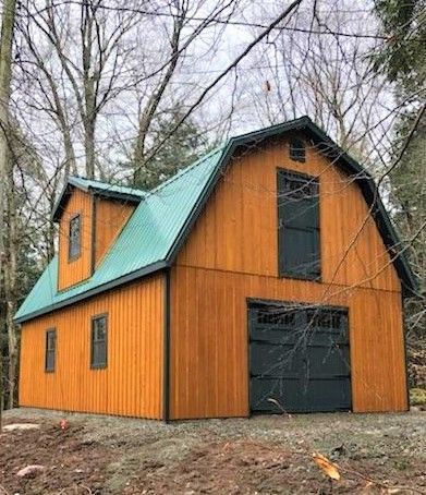 Barn with orange siding, teal roof, and dark green garage door, surrounded by trees.