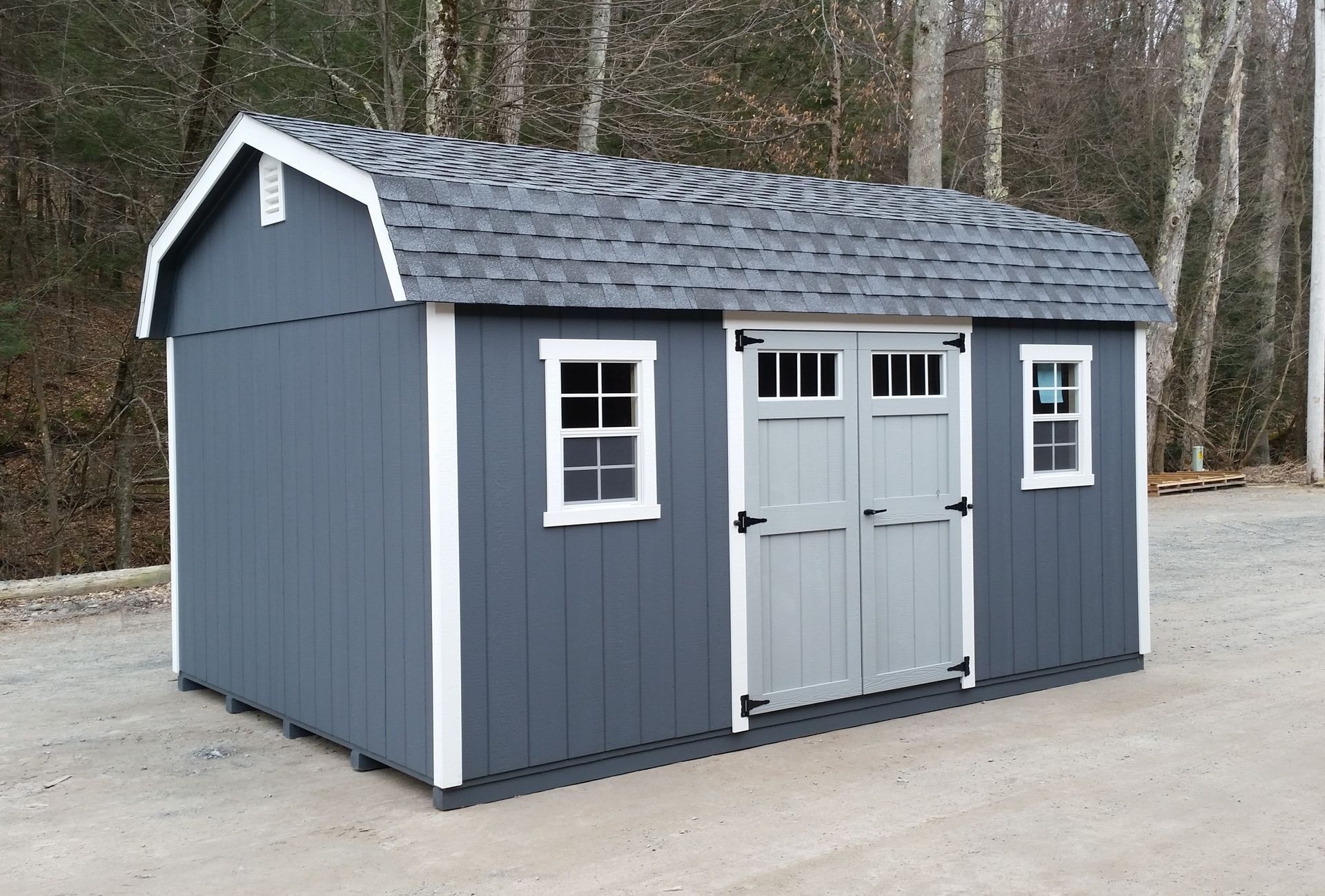 Gray shed with white trim and door, set against a backdrop of trees.