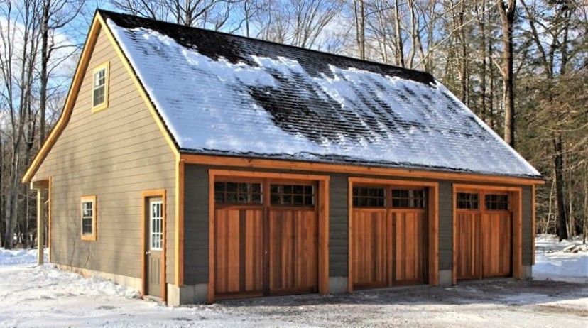 Three-car garage with brown wood doors and snow-covered roof on a winter day.