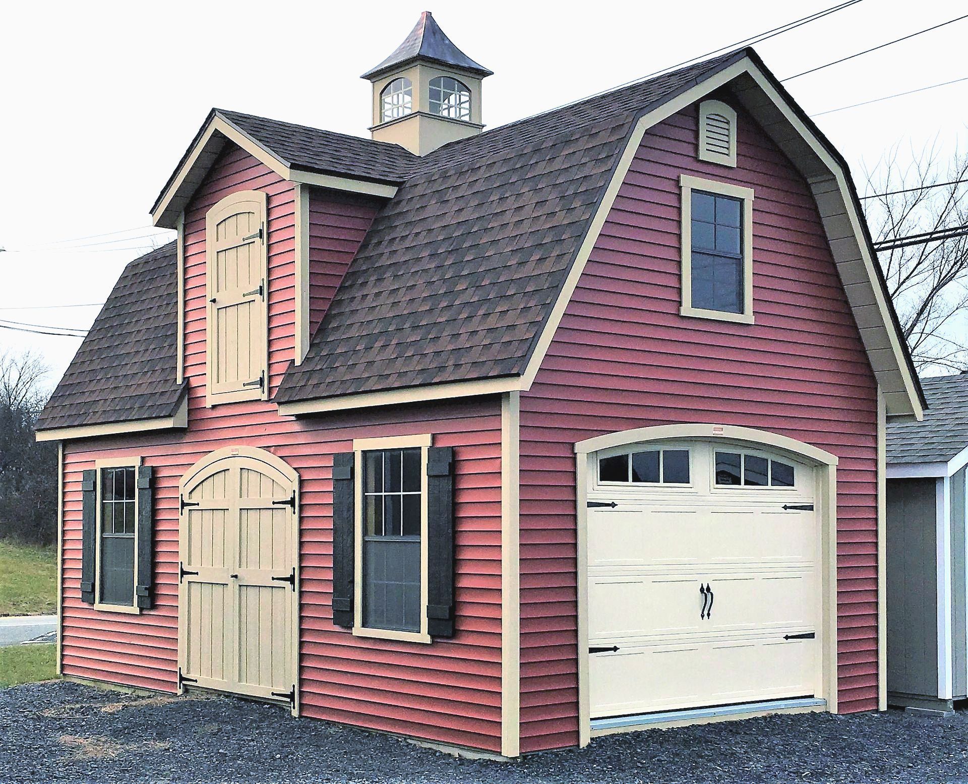 Red barn-style shed with beige trim, a garage door, and a cupola.
