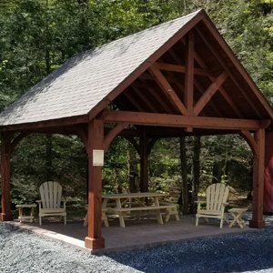 Wooden pavilion with seating, in a wooded area.