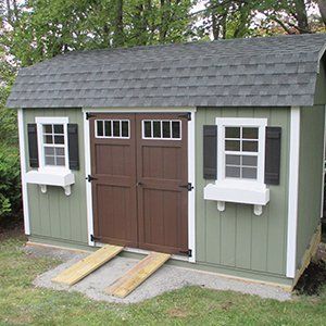 Green shed with brown doors and windows with black shutters, two wooden ramps lead to the door.