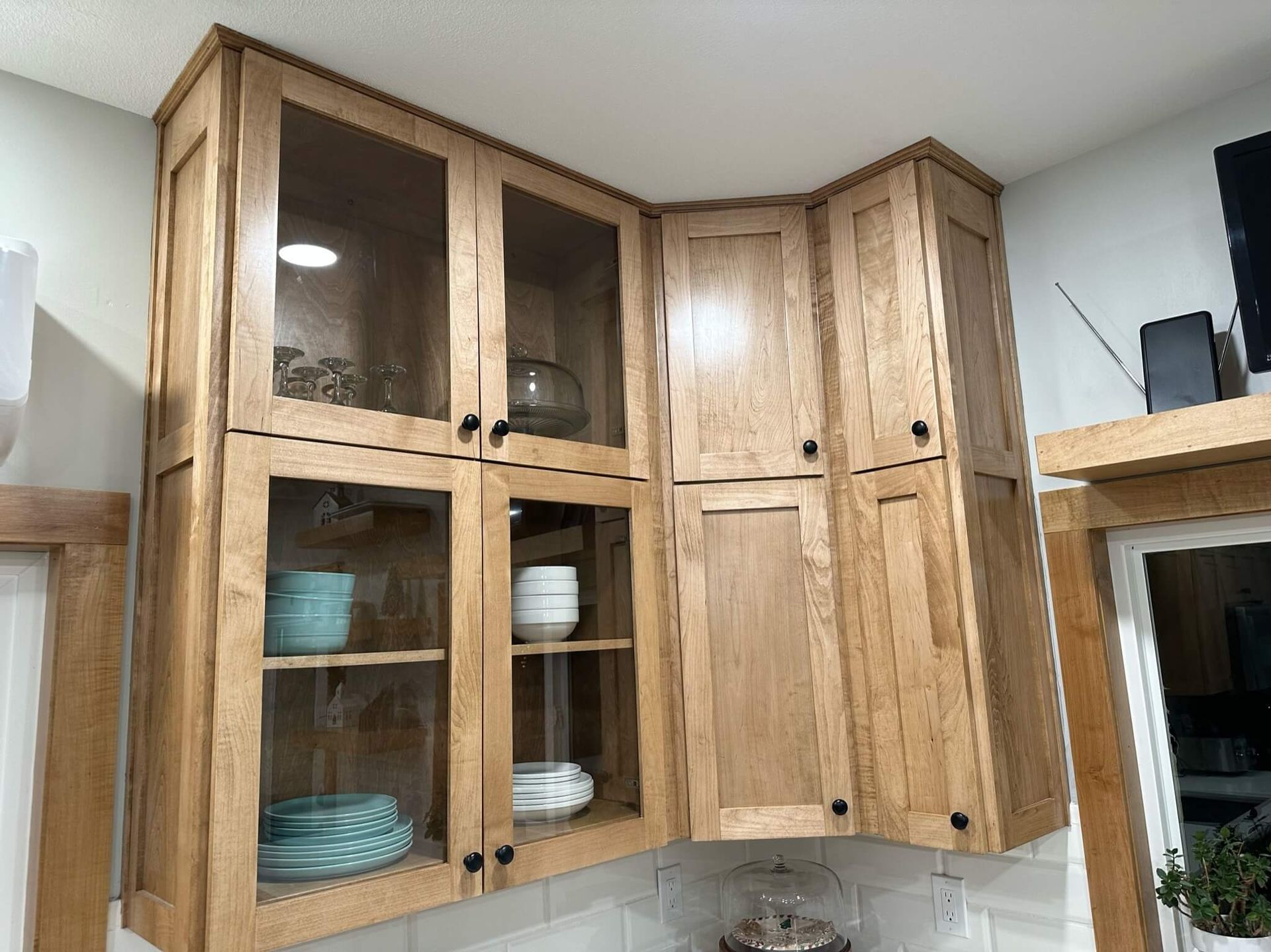 Corner upper kitchen cabinets with glass-front doors on the left and solid wood doors on the right.
