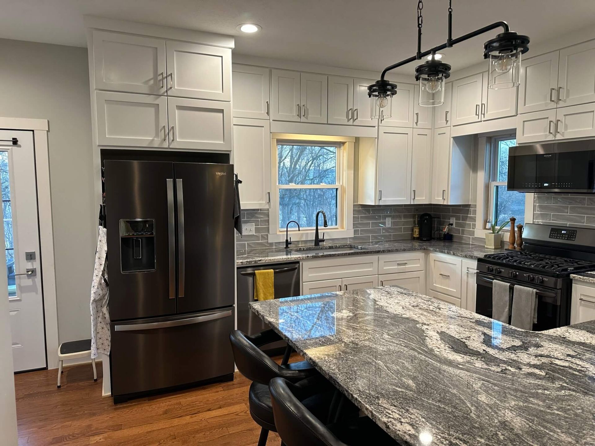 A modern kitchen featuring white cabinets, dark granite countertops, stainless steel appliances, and a central island.