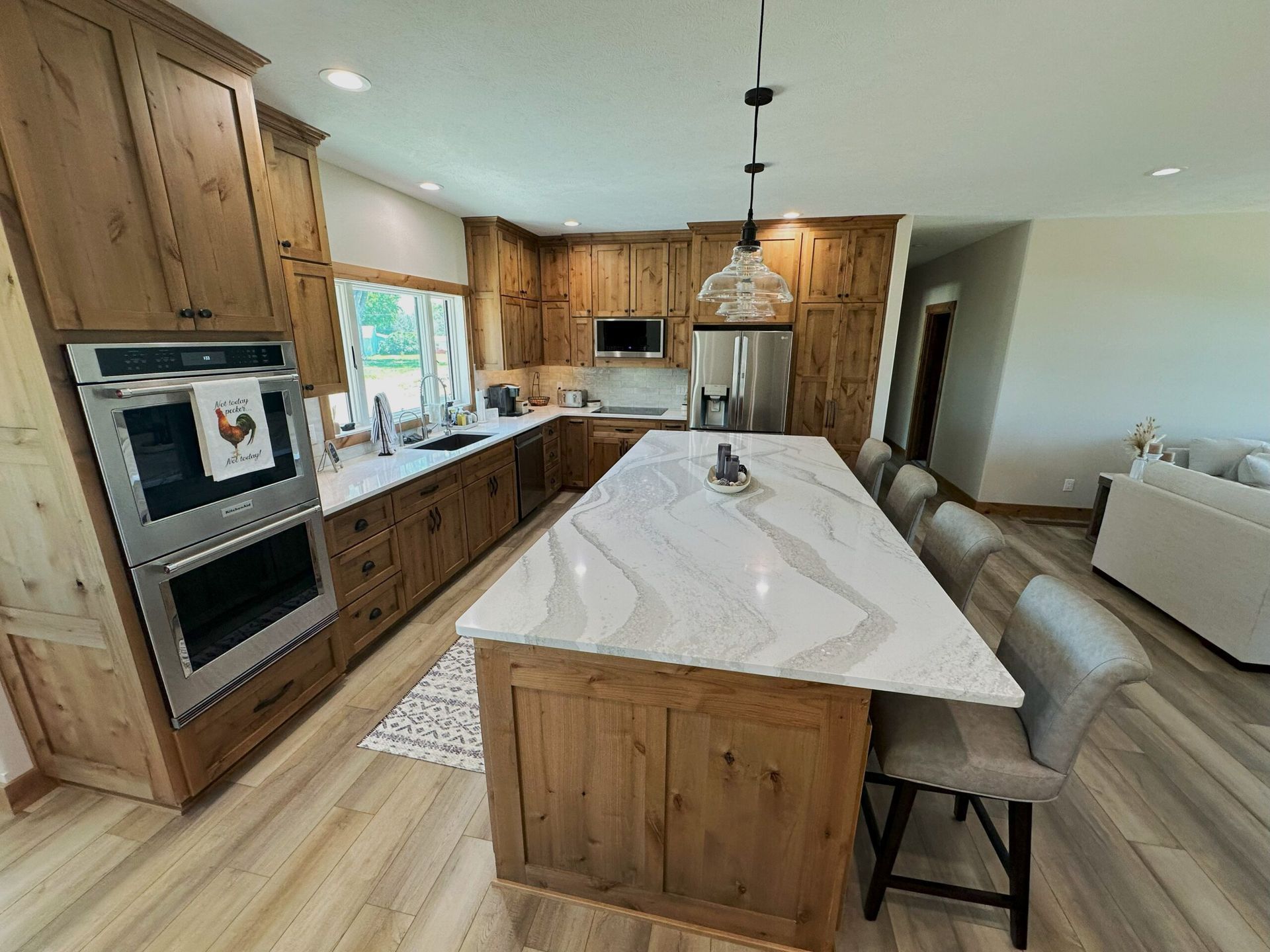A spacious, modern kitchen featuring wooden cabinets, a large white-veined marble island, and stainless steel appliances.