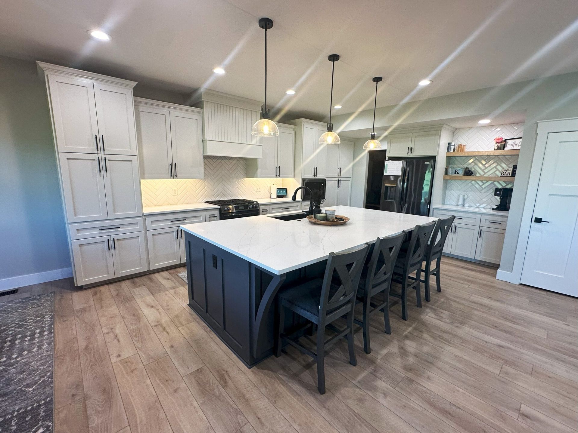 Modern kitchen with a large dark blue island, white cabinets, light wood floors, and three pendant lights.