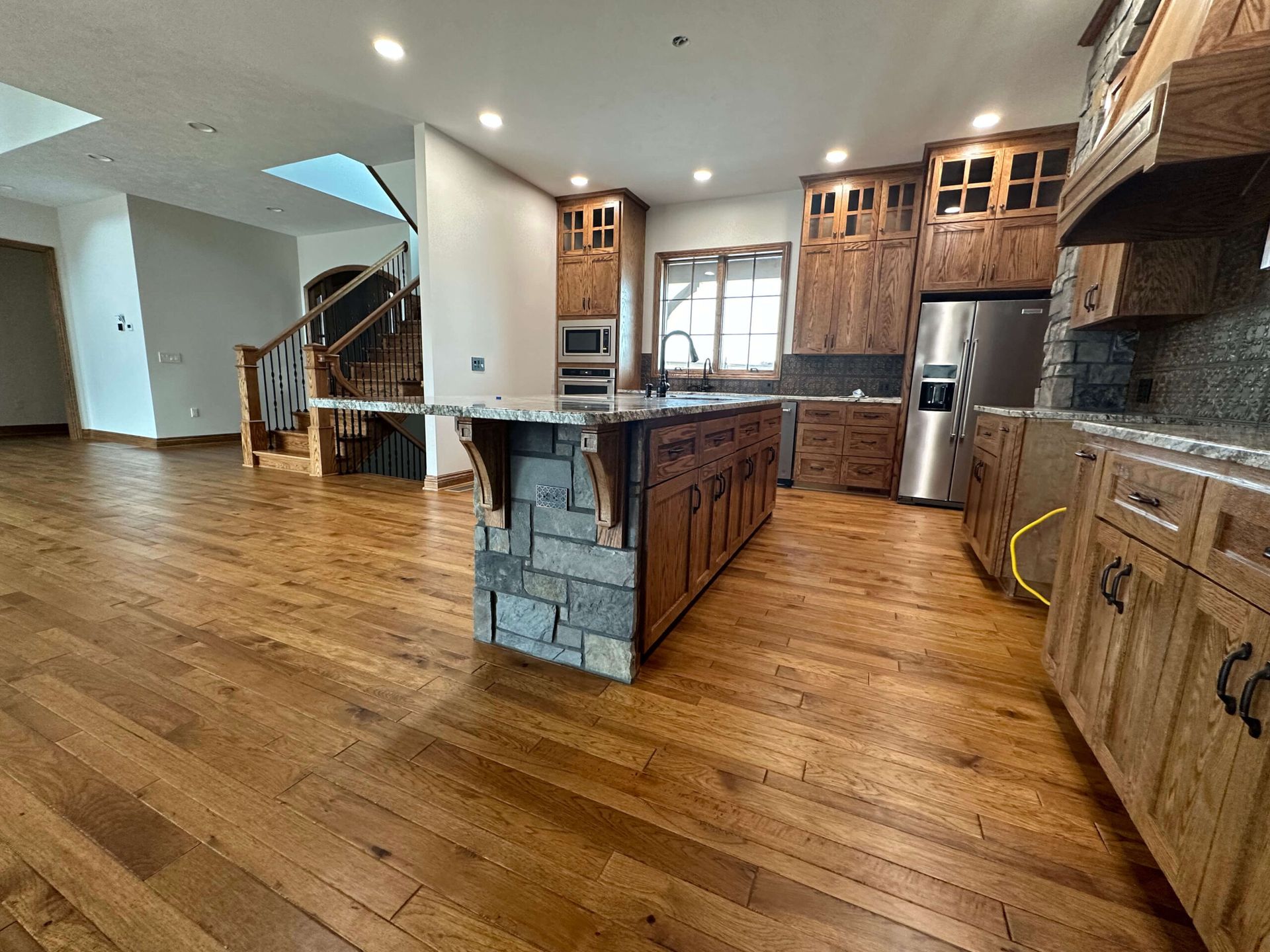 A kitchen featuring medium-tone wood cabinets, a stone-based island, and matching wood flooring, with a staircase nearby.